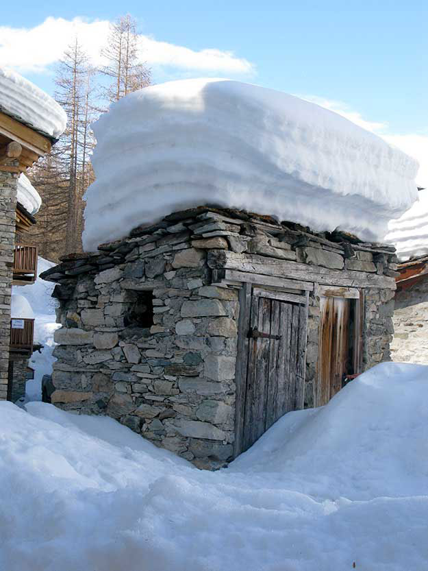  בתי אבן נמוכים מכוסים בשלג שנערם כמו מצנפות שינה כבדות על גגות הרעפים